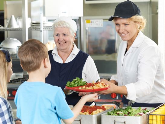 Mitarbeitende schöpft gesundes Mittagessen für Schüler Mitarbeitende schöpft gesundes Mittagessen für Schüler